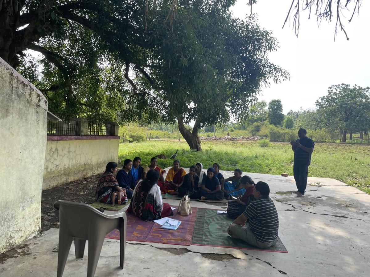 Community members seated under a tree for a village meeting
